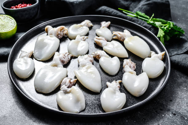 istock Raw mini cuttlefish with rosemary and parsley on a plate. Black background. Top view 1206007561