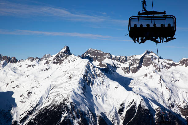 Silhouettes of people with skis and snowboards on a chairlift against a mountain panorama on a clear Sunny day. Ischgl Austria stock photo