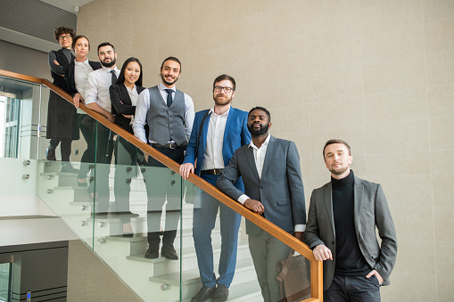 Confident multi-ethnic business team members standing in row on stairs and looking at camera