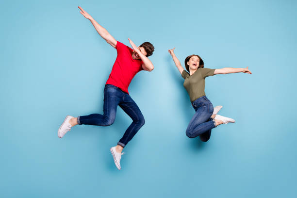 full-size-foto von funky verrückt zwei verheiratete studenten spaß springen mann führen dab tänzer frau heben hände tragen grün rot t-shirt jeans jeans isoliert blau farbe hintergrund - dab tanz stock-fotos und bilder