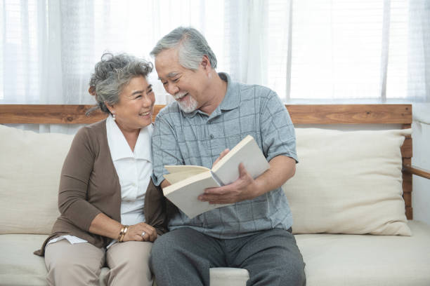 自宅で一緒に本を読んでソファに座っている高齢のシニアアジアのカップル。 - senior adult relaxation sofa reading ストックフォトと画像