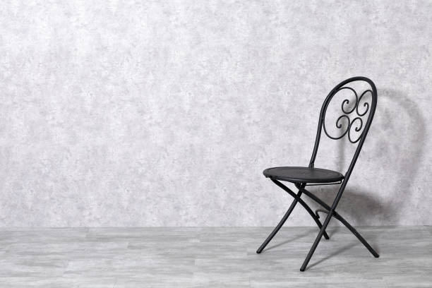 Vintage metal chair on green grass in sunlight. Outdoor furniture detail with strong shadow and autumn leaves.