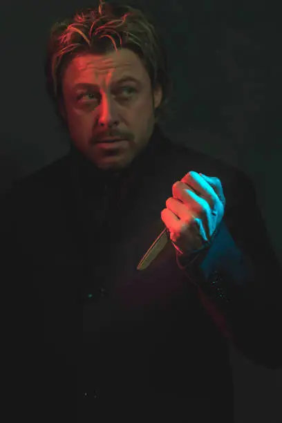 Photo of Scary man with scissors in hand illuminated by red and blue light.