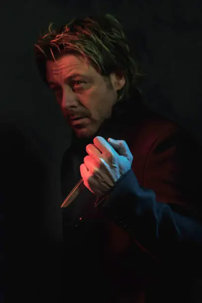 Photo of Scary man with scissors in hand illuminated by red and blue light.
