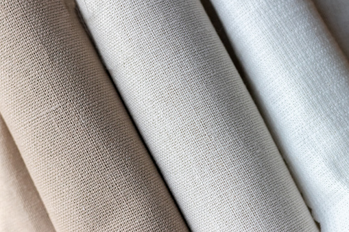 Diagonal textural background of three types of natural linen fabric, rolled up. Selective focus. Closeup view
