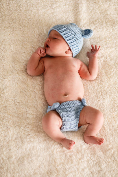 Direct above shot of a sleepy cute newborn lying on a bed with blue knitted clothes.