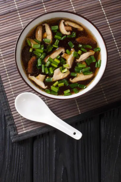 Photo of Vegetarian miso soup with shiitake mushrooms and green onions close-up in a bowl. Vertical top view