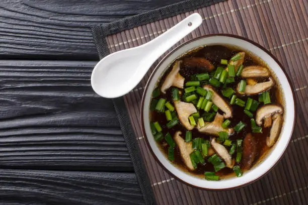 Photo of Traditional Japanese soup with shiitake mushrooms and green onions close-up in a bowl. Horizontal top view