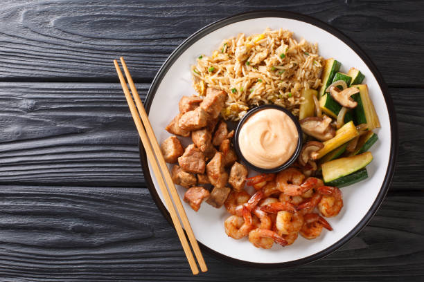 Serving hibachi of rice, shrimp, steak and vegetables served with sauce closeup in a plate. Horizontal top view Serving hibachi of rice, shrimp, steak and vegetables served with sauce closeup in a plate on the table. Horizontal top view from above prawn grilled seafood prepared shrimp stock pictures, royalty-free photos & images