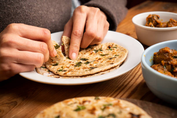 Woman having food, Potato curry (Kashmiri dum aloo) with chapatti (roti) on table.