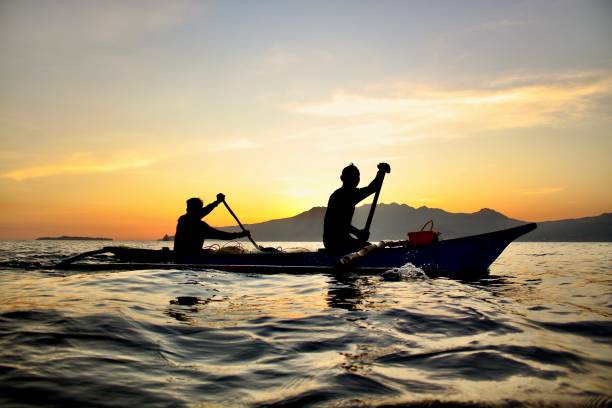 Silhouetted Boaters A pair of boaters rowing by as the sun sets behind them. zambales province photos stock pictures, royalty-free photos & images