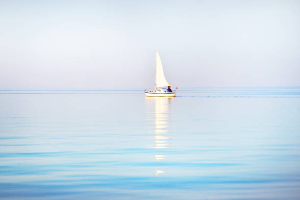 yate de sloop blanco navegado en un mar báltico abierto al atardecer. reflejos sobre el agua, colorido cielo nocturno y luz solar cálida. letonia - sea water single object sailboat fotografías e imágenes de stock