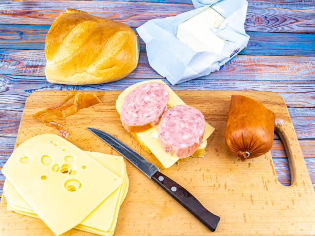 Sandwich with sausage and hard cheese on a cutting board. Butter with bread. Kitchen knife. Kitchen table. Place for text.