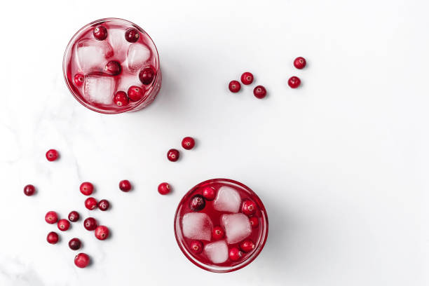cranberry-cocktail in kristallgläsern mit eis, das von beeren auf weißem marmorhintergrund verziert ist. flache laien-stil. kopieren sie den speicherplatz. - cranberry stock-fotos und bilder