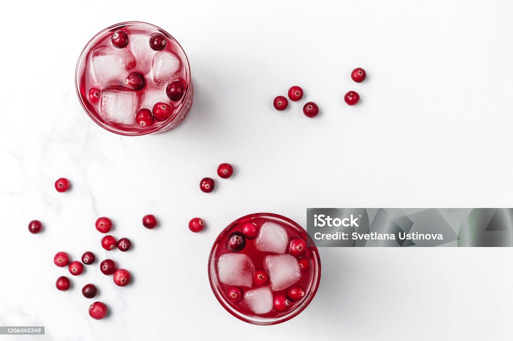 Cranberry cocktail in crystal glasses with ice decorated by berries on white bright marble background. Flat lay style. Copy space. Cranberry cocktail in crystal glasses with ice decorated by berries on white bright marble background. Copy space. Flat lay style. Cranberry Stock Photo