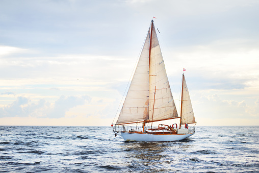 Vintage wooden two mast yacht (yawl) sailing in a open sea on a clear day. Waves and white clouds