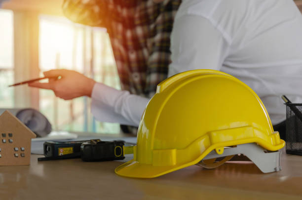 istock yellow safety helmet on workplace desk with construction worker team meeting and planning about building plan in office center at construction site, real estate, engineering and contractor concept 1206048745