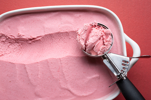 Scoop of raspberry ice cream close-up on a red table. Above view of homemade berries ice cream. Fresh summer dessert. Red ice-cream details.