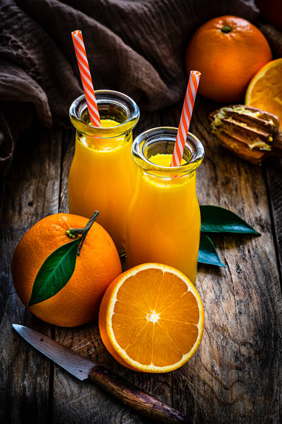 high angle view of two homemade orange juice bottles on rustic wooden table - freshly squeezed orange juice imagens e fotografias de stock
