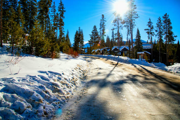 A plowed but icy winter road through a rural neighborhood in Colorado near Winter Park on a bright sunny day.