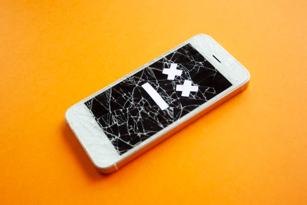Broken smartphone with cracked destroyed screen on orange background with sad smile. Broken phone service, recovery and repair concept, symbol from side.