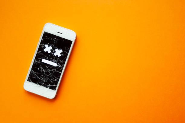 Broken smartphone with cracked destroyed screen on orange background with sad smile. Broken phone service, recovery and repair concept, symbol top view copyspace. Broken smartphone with cracked destroyed screen on orange background with sad smile. Broken phone service, recovery and repair concept, symbol top view copyspace. phone repair stock pictures, royalty-free photos & images