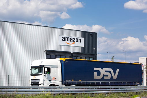 Raunheim, Germany - August 21, 2019: Facade and logo of amazon logistics center in Raunheim-Moenchhof, Germany. Amazon.com, Inc. is an American electronic commerce and cloud computing company and the largest Internet retailer in the world as measured by revenue and market capitalization. In the foreground a passing truck of German freight transportation company DSV
