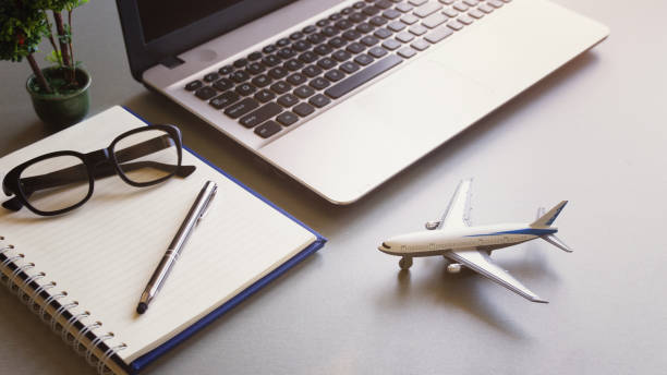 View home desk with plant, notebook , pen and eyeglasses ,airplane model flight schedule concept vacation planning online
