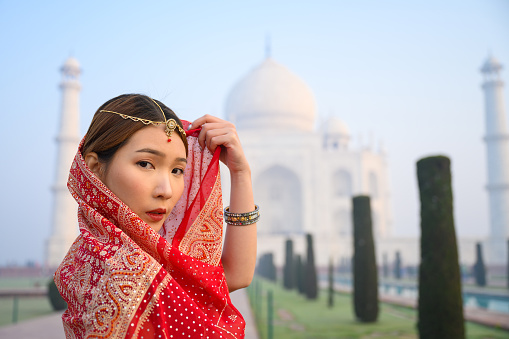 Portrait of young woman in red saree indian traditional dress against Taj Mahal, Agra, India