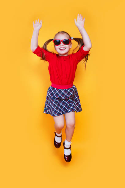 黄色の背景にジャンプ赤いサングラスで面白い小さな女の子 - glasses child red hair little girls ストックフォトと画像
