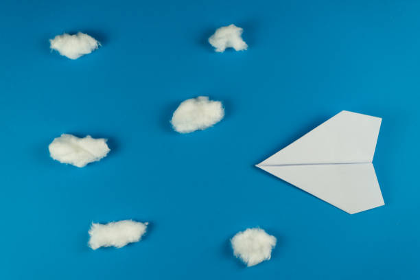 istock Handmade white paper plane on blue background with clouds made with cotton 1206068305
