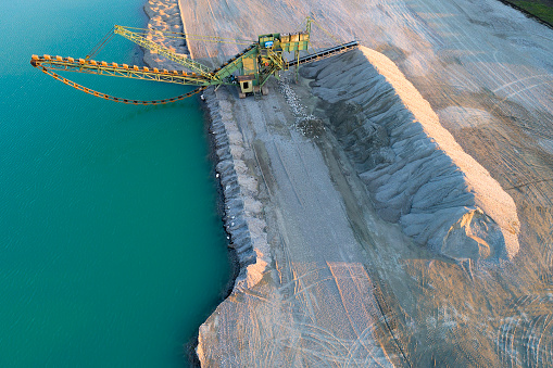 Gravel mining machine stands on the shore of the lake, aerial view.