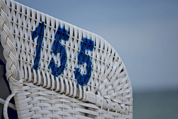 Number 155 stencilled in blue on a white painted wicker beach chair overlooking the ocean in close up