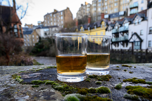 Scotch single malts or blended whisky spirits in glasses with old houses of Edinburgh city on background, Scotland, UK