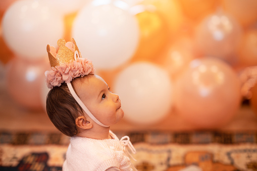Cute little baby girl while sitting on birthday party background