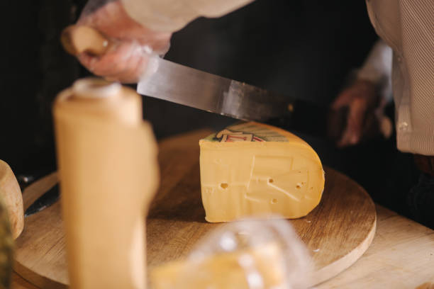 Man slicing a cheese on wooden board. Cheese shop.