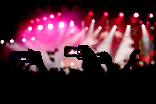 Silhouette of hands using smartphones to take pictures and videos at live music show