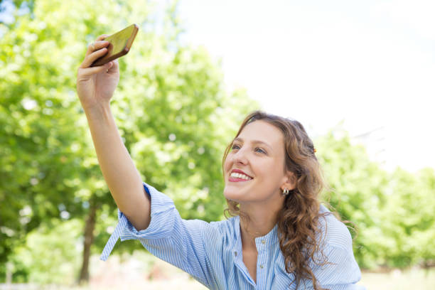 istock Smiling young woman taking selfie with smartphone in spring park 1206140047
