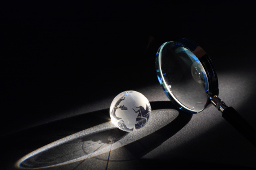 Magnifying glass and globe on dark background with beam of light