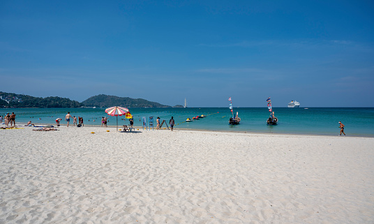 Aerial summer view of Patong Beach in Phuket, Thailand. People are walking along the beach, swimming or laying down resting on the white sand beach.