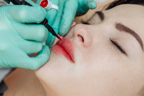 istock Permanent makeup on lips. Cosmetologist applying tattoo with machine 1206145252