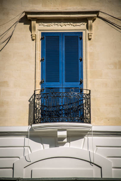 Decorative ironwork, of circles framed within a square,  on a window which looks out over a view of pine trees, tiled roof, the Mediterranean Sea and the horizon.  Santa Margherita di Pula, Sardinia, Italy.