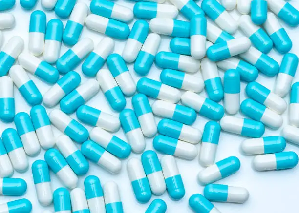 Photo of Blue-white capsule pills on white table. Full frame of capsule drug pills. Pharmacy product. Pharmaceutical production concept. Pharmaceutics. Medicine use in hospitals and pharmacies. Healthcare.