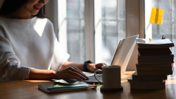istock Cropped shot of young designer woman using computer laptop while sitting at the modern working desk with sun light through the window as background. 1206150175