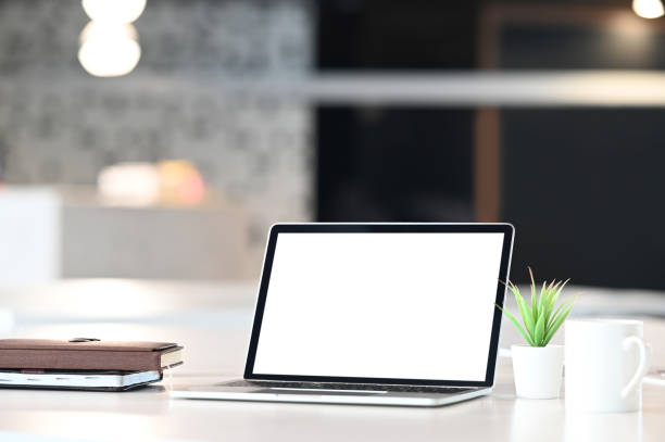 istock Computer laptop with white blank screen, potted plant, coffee cup and stack of books putting together on modern working desk with blurred background. 1206150258