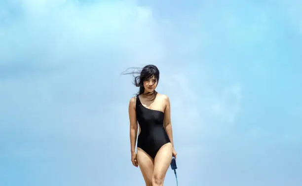 The beautiful woman wearing black swimsuit,model posing,sky background,blurry light around