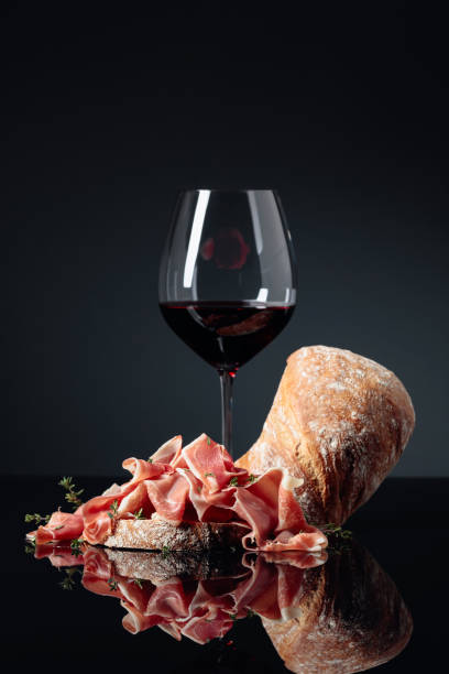 Prosciutto with ciabatta, red wine and thyme on a black background. Prosciutto with ciabatta, red wine and thyme on a black reflective background. prosciutto stock pictures, royalty-free photos & images