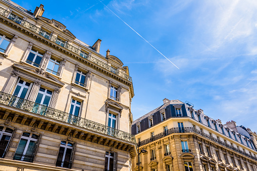 Low angle view of typical Haussmannian style residential buildings in the chic neighborhoods of Paris, France, on a sunny day against blue sky.