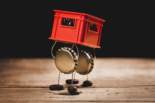 Crown cork miniature figures carrying a red beer or beverage crate, hilarious conceptual scene for drink promotion Crown cork miniature figures carrying a red beer or beverage crate, hilarious conceptual scene for drink promotion beer crate stock pictures, royalty-free photos & images