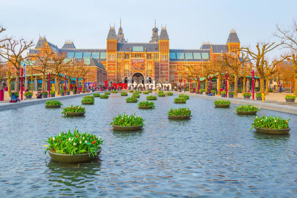 Amsterdam, Netherlands - March 31, 2016: Water and colorful tulip flowers, Rijksmuseum and people in front of writing, I amsterdam, Museumplein, Holland